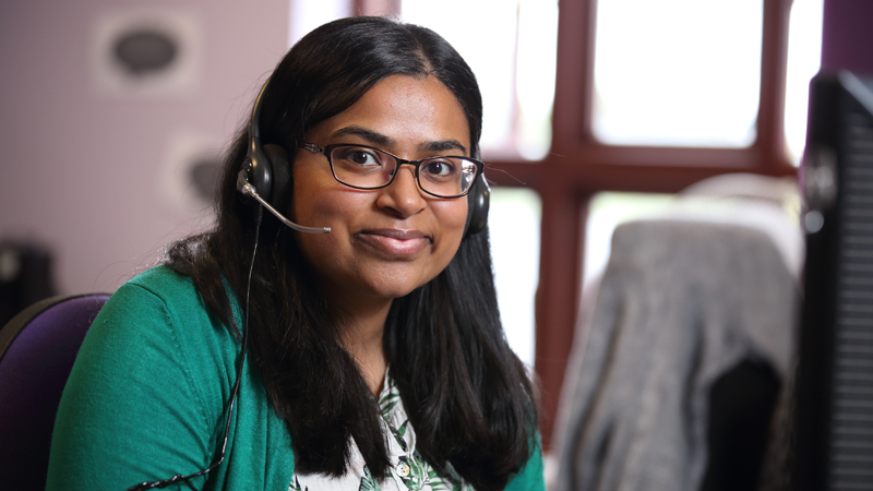 Hema, from our Stroke Support Helpline, sits, smiling, at her desk with her telephone headset on as if waiting to answer a call.