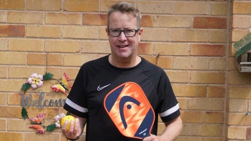 Stroke survivor, Jeremy, poses holding up a Pickleball paddle and ball.