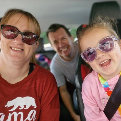 Emily, a childhood stroke survivor, smiles from the front seat of the car with her parents