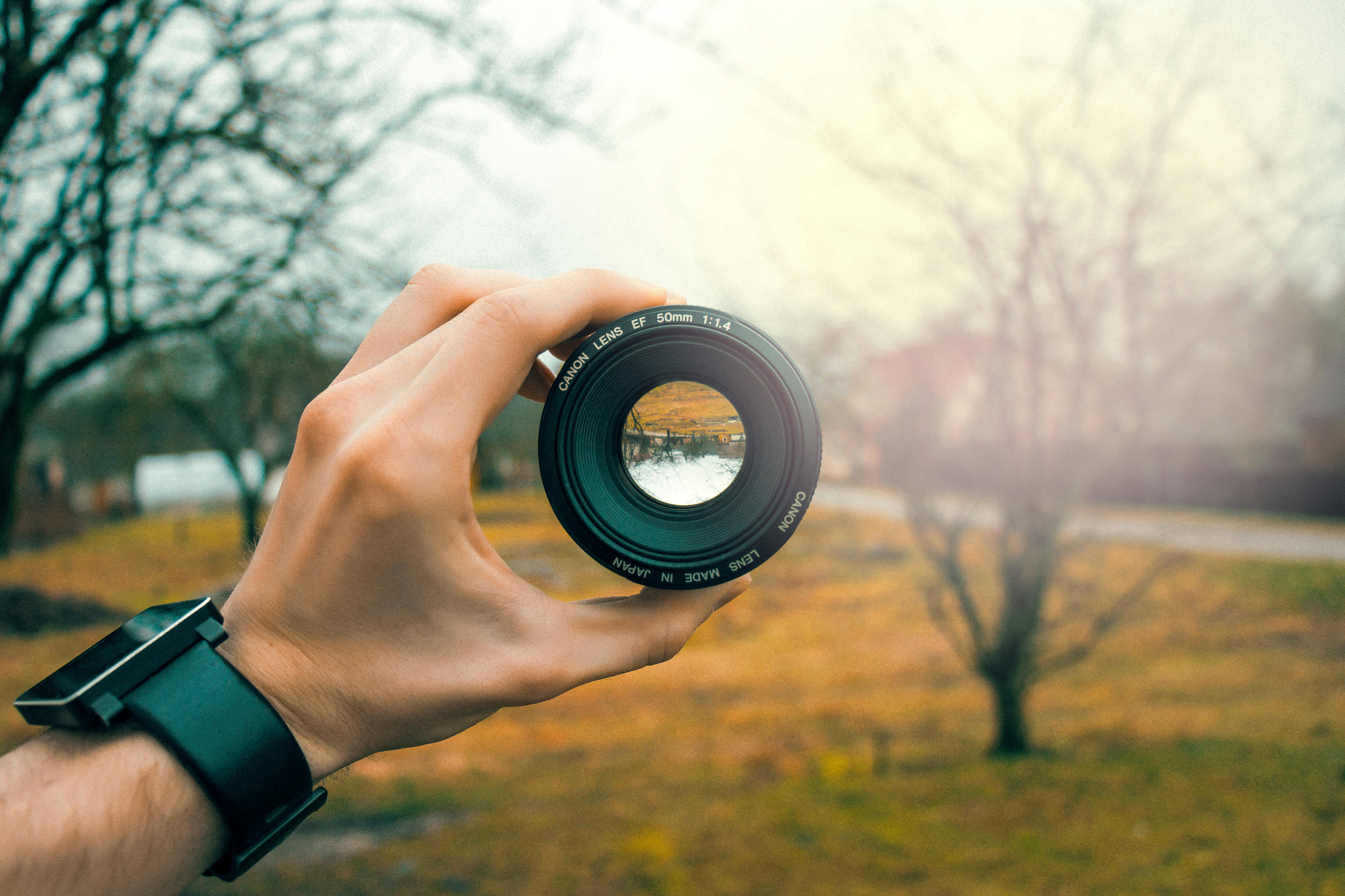 A hand holds a camera lens up towards the horizon, it shows an upside down view of the horizon, but a much sharper image.
