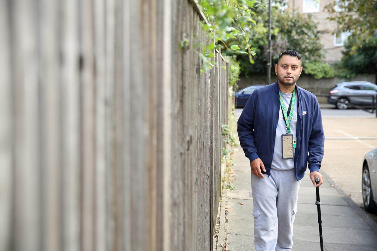 A man walking along a street using a walking stick.