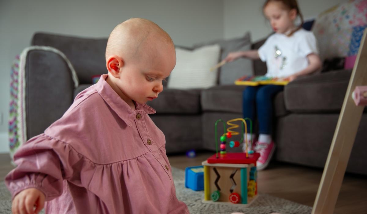 Anna, a childhood stroke survivor, plays on the floor while her sister plays on the sofa behind her