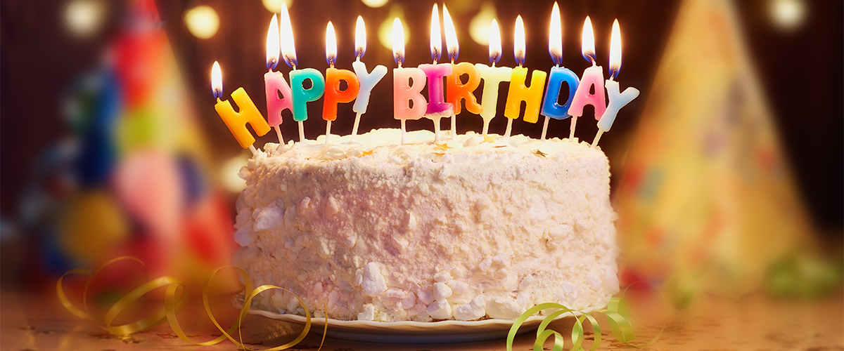 A birthday cake with colourful candles on top in the shape of letters which spell 'Happy Birthday'.