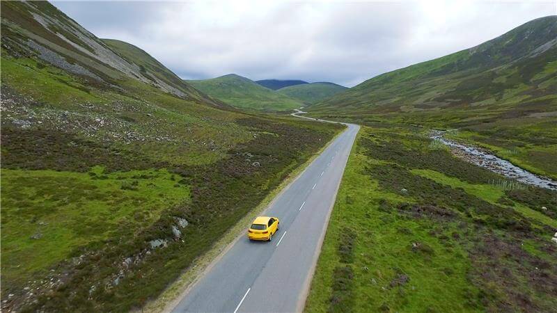 A photo showing a lone little yellow car driving on a road through Glenshee Aberdeen