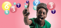 A woman smiling and holding up one finger in front of lottery number balls