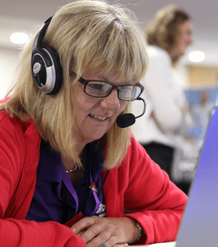 Photo of a member of the online helpline team with a headset on, looking at her laptop and smiling