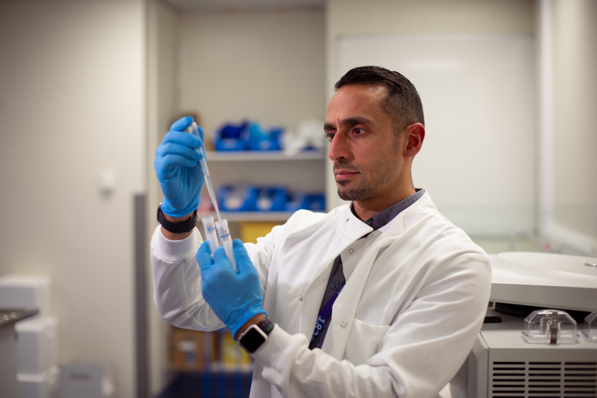 Dr Ali, in the lab, looks at a syringe and vial