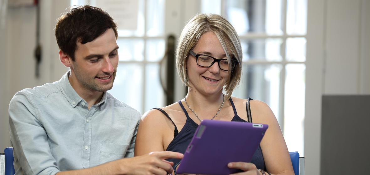 A man and a woman looking at and interacting with a digital tablet device.