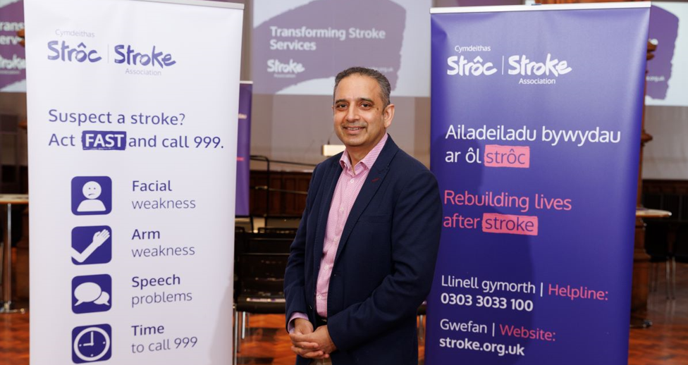 Shakeel Ahmad standing next to FAST campaign banners in Welsh