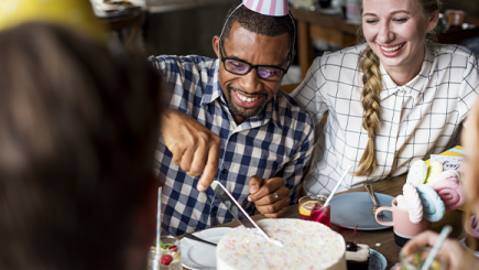 People in birthday hats cutting a cake